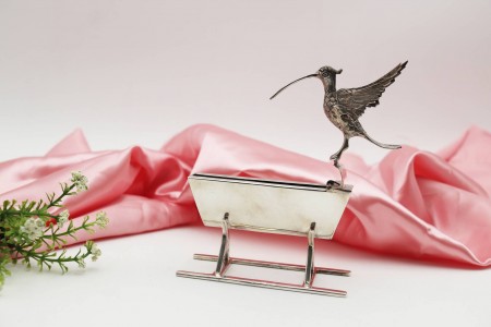  Paliteiro em prata representando um pássaro de asas abertas junto a bebedouro em movimento.